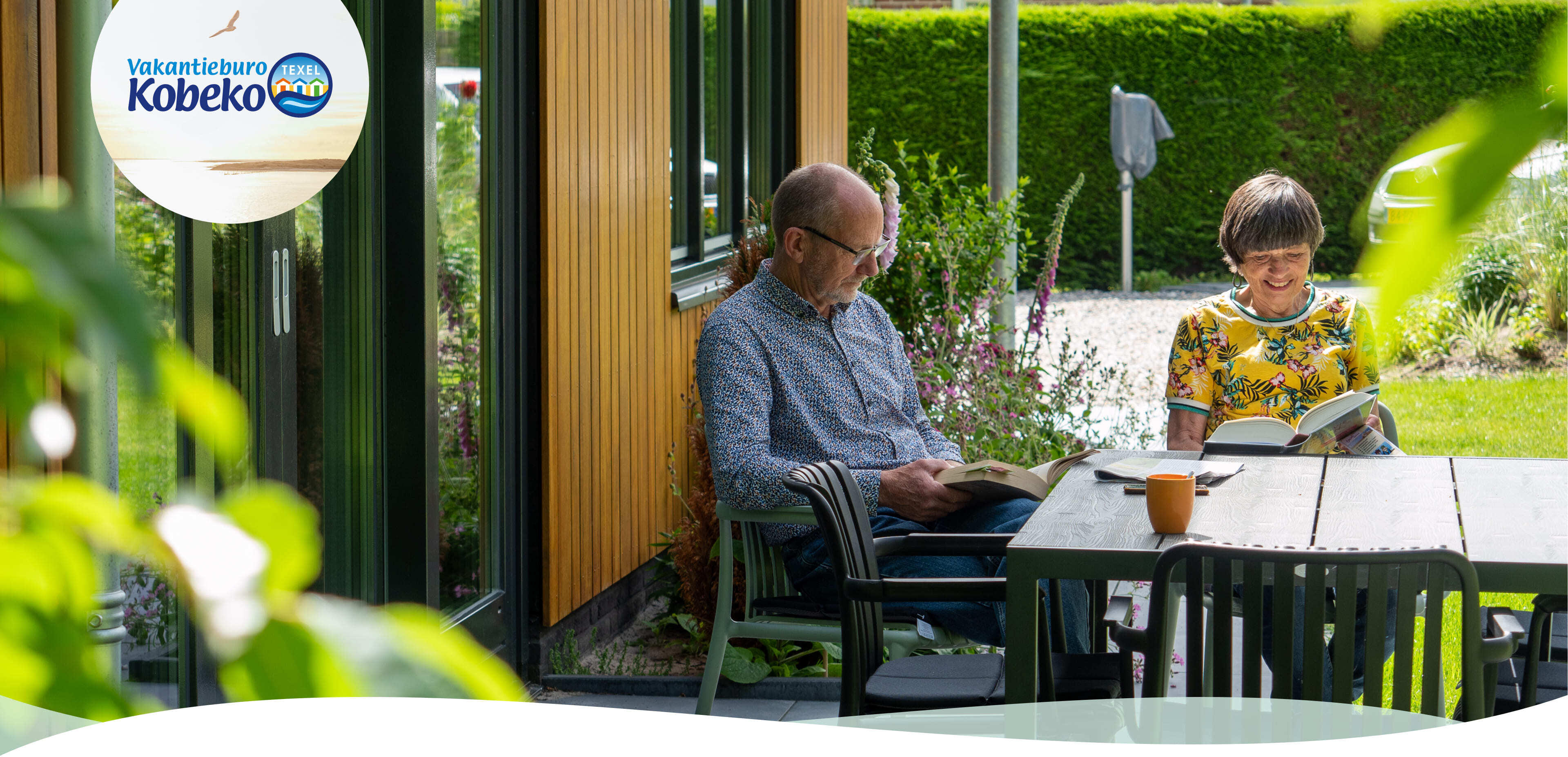 Een man en een vrouw zitten buiten aan een tafel boeken te lezen naast een modern gebouw, omringd door een tuin en groen. Misschien zijn ze bezig met het verkennen van websites of online diensten op hun apparaten, terwijl ze genieten van de rustige omgeving.